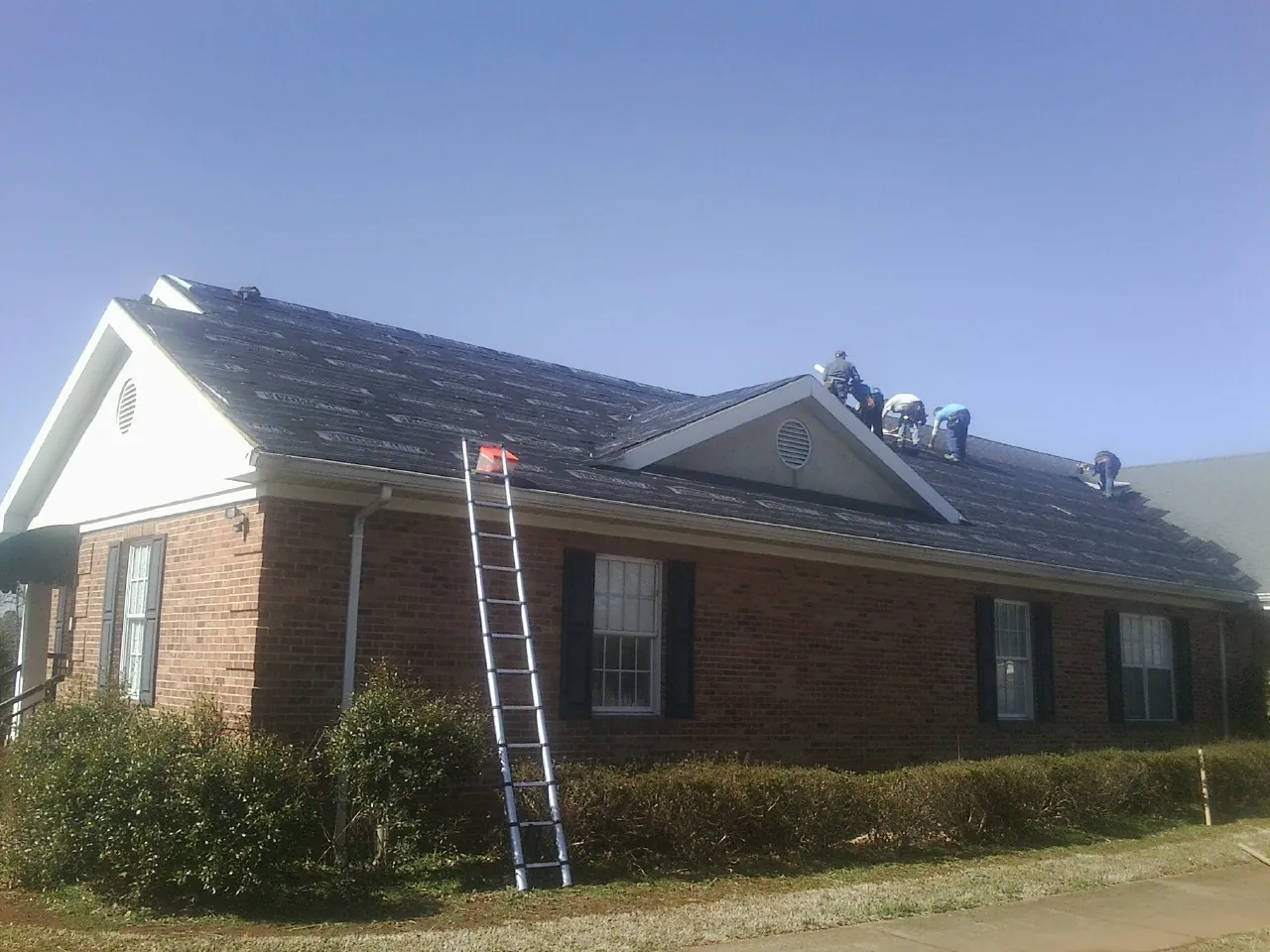 Crew tearing shingles off a brick ranch roof with a ladder set — Emergency Roof Repair work by our crew in Valley Lee