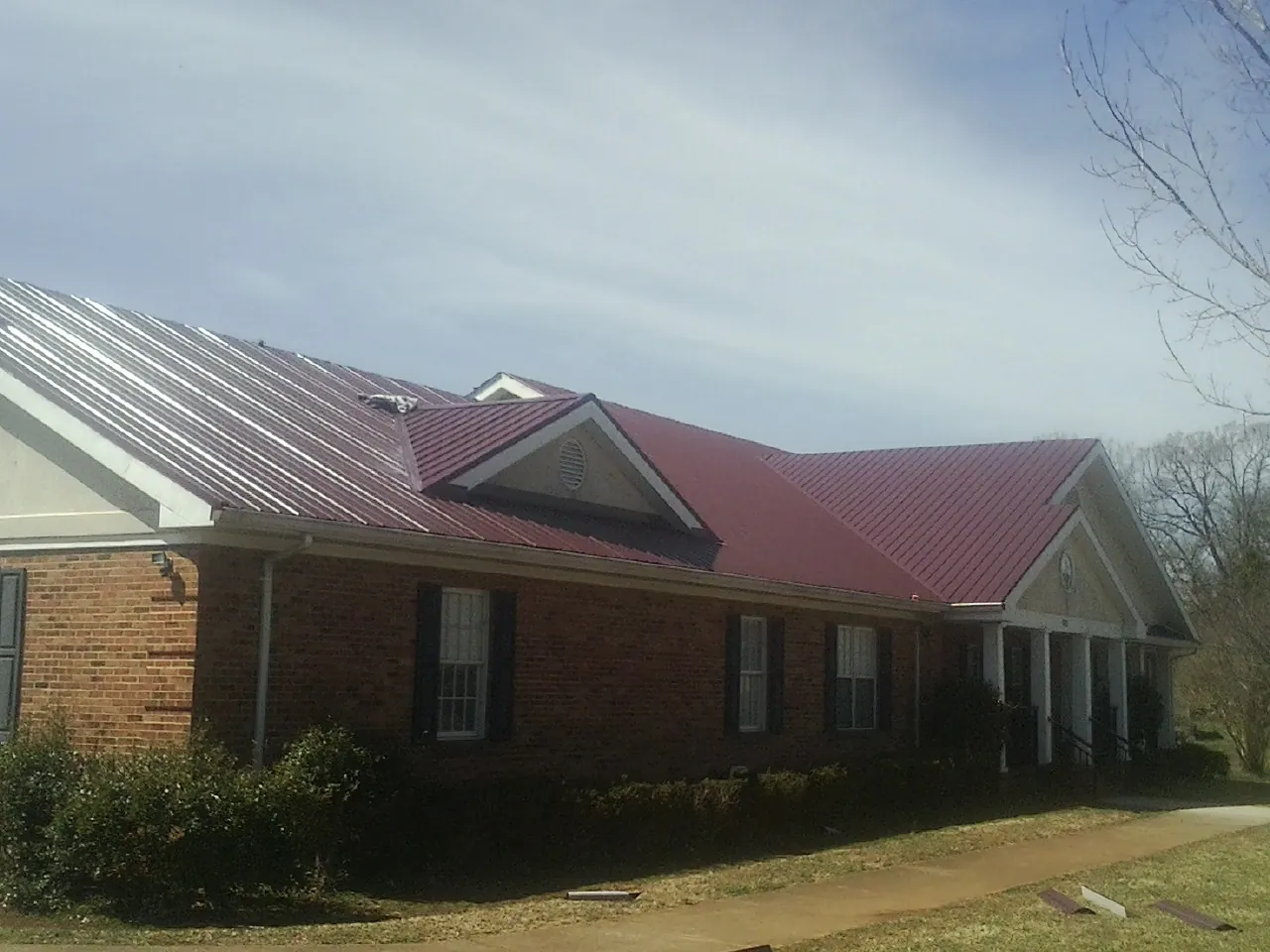 Red metal roof with gabled entries on a long brick building, from a Hail Damage Roof Repair job in Valley Lee