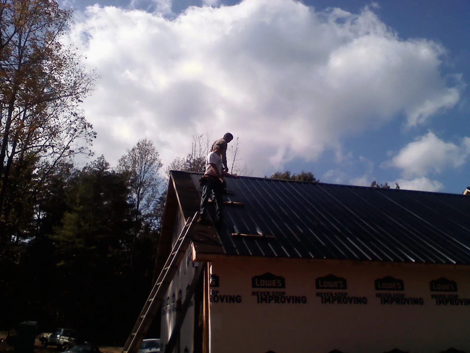 Roofer fastening dark metal panels high against a cloudy sky, from a Roof Inspection job in Valley Lee
