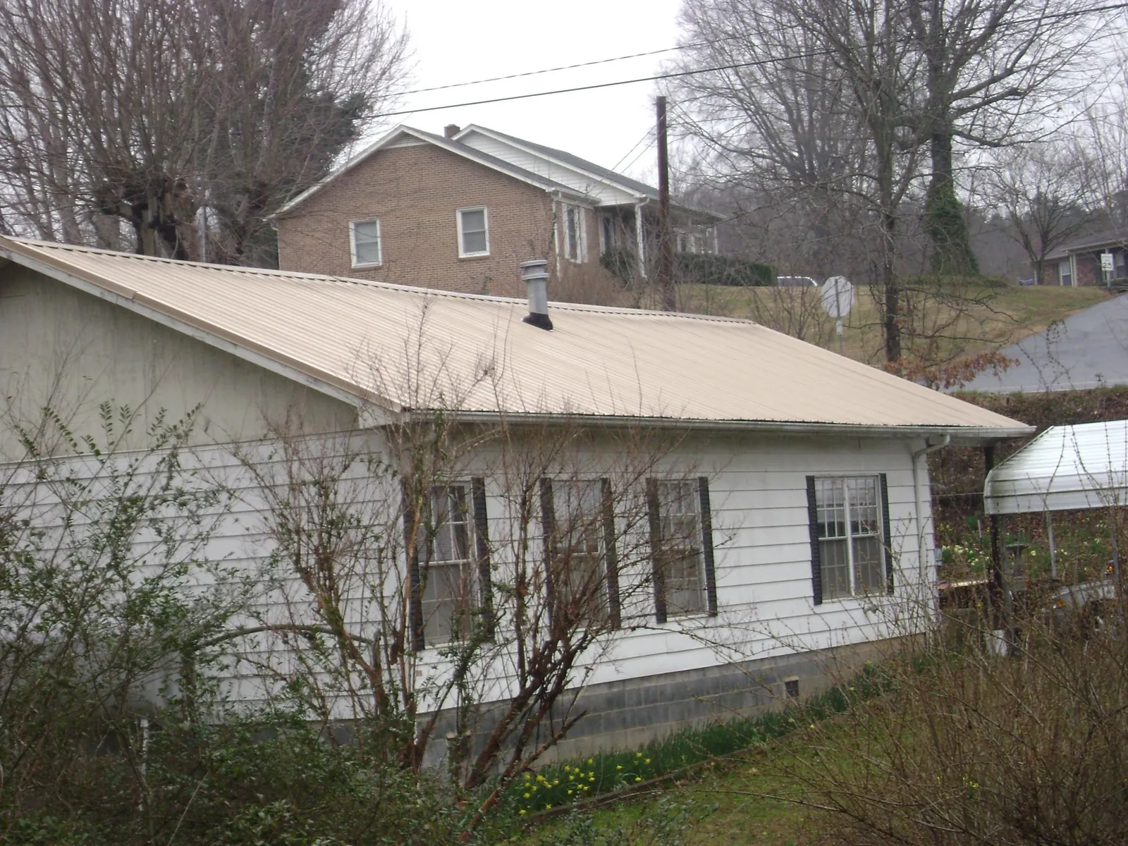 Tan metal roof on a white sided house set into a hillside — Commercial Roofing by Roofing Brothers in Valley Lee